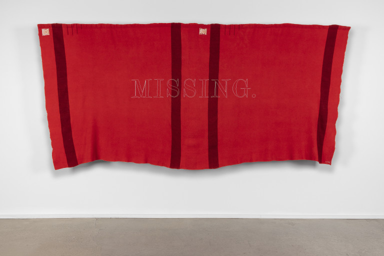 	Double Hudson’s Bay chief trade blanket in red with black stripes. The word *Missing.* has been sewn onto its surface using tiny glass beads. Photograph by Kevin McConnell.